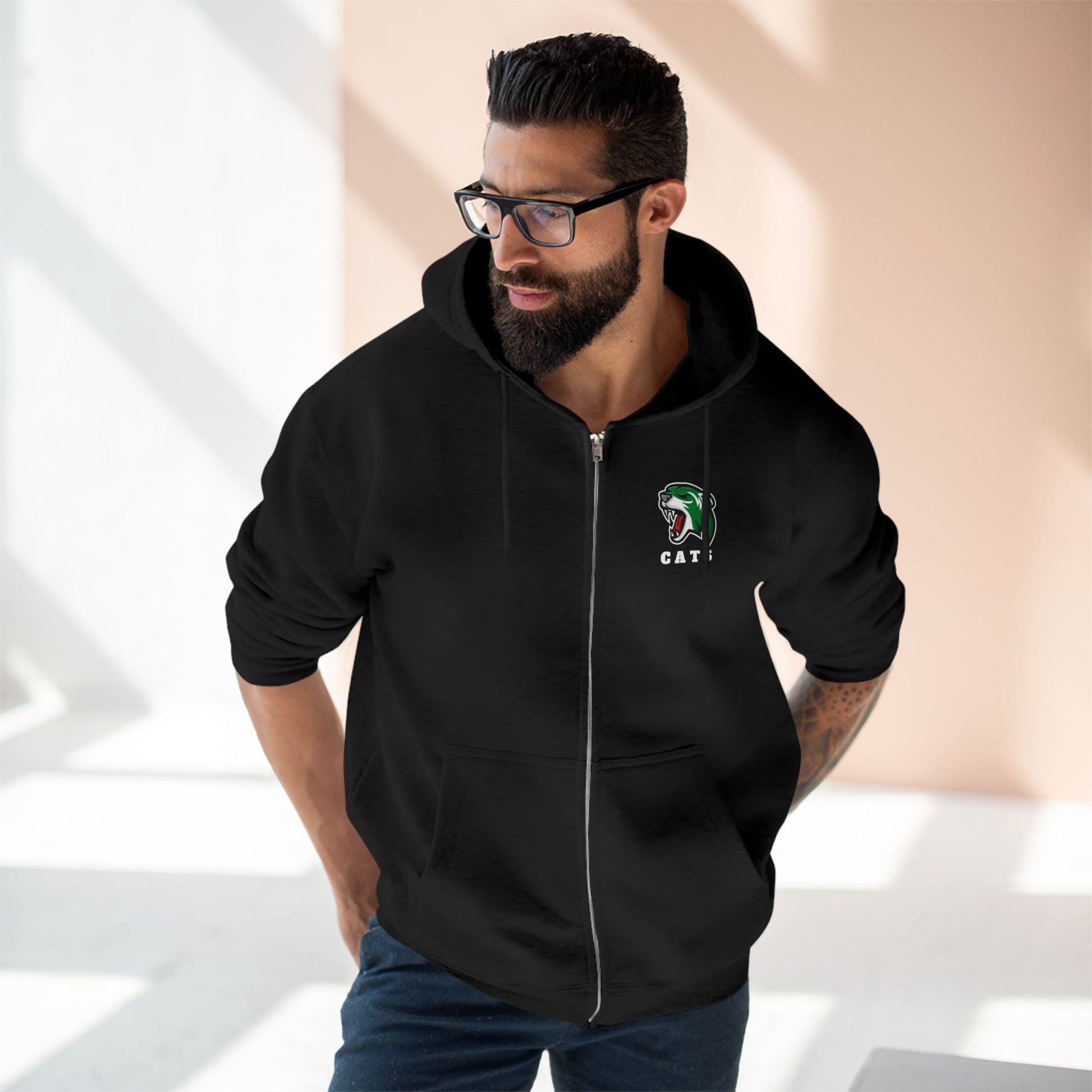Man with brown skin and black hair/beard wearing glasses, Black Noah Boucher Toronto Fisher Cats Zip Hoodie, and jeans
