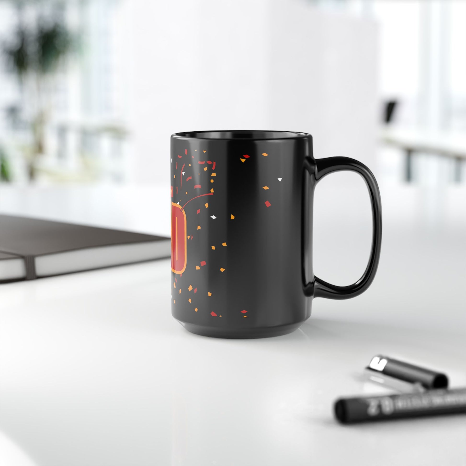 Side view of black mug with red and yellow '#1 Hockey Dad' text, Boston Harrier's logo and confetti design against a white table with a pen and notepad
