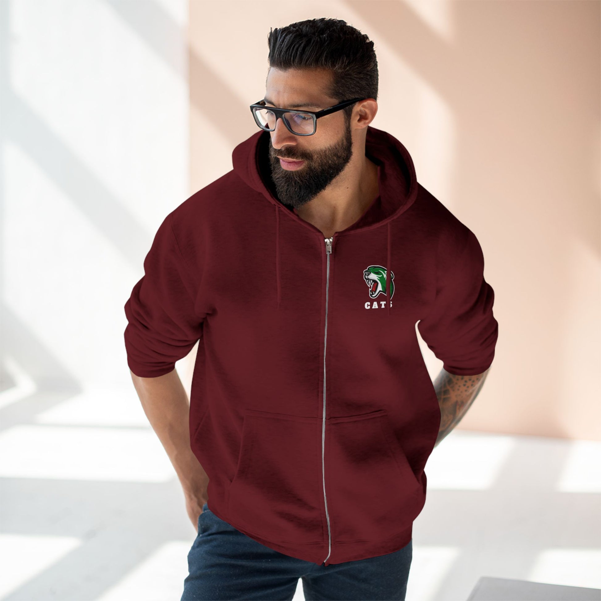 Man with brown skin and black hair/beard wearing glasses, Burgundy Noah Boucher Toronto Fisher Cats Zip Hoodie, and jeans
