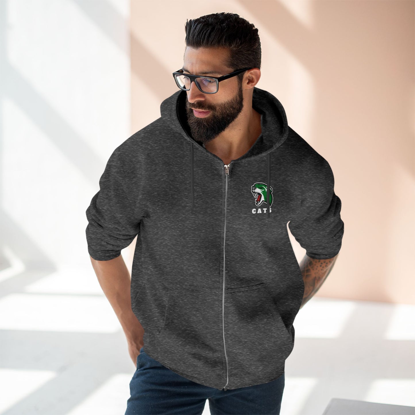 Man with brown skin and black hair/beard wearing glasses, Charcoal Grey Noah Boucher Toronto Fisher Cats Zip Hoodie, and jeans. 