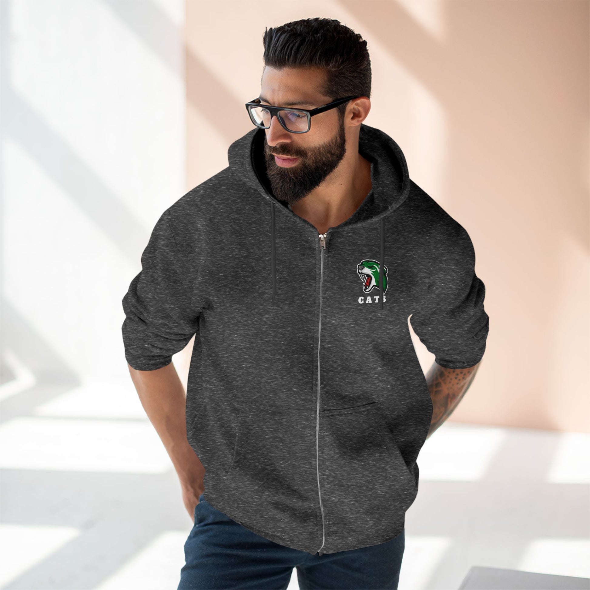 Man with brown skin and black hair/beard wearing glasses, Charcoal Grey Noah Boucher Toronto Fisher Cats Zip Hoodie, and jeans. 