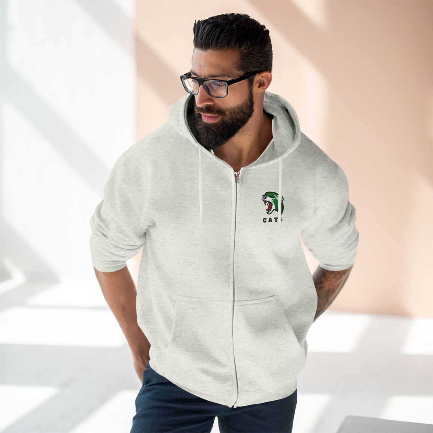 Man with brown skin and black hair/beard wearing glasses, Oatmeal Heather Noah Boucher Toronto Fisher Cats Zip Hoodie, and jeans