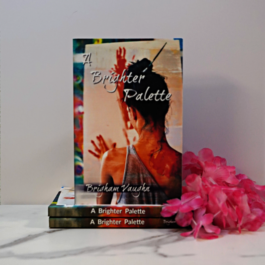 Signed paperback book titled 'A Brighter Palette' by Brigham Vaughn with pink flowers on a white surface.