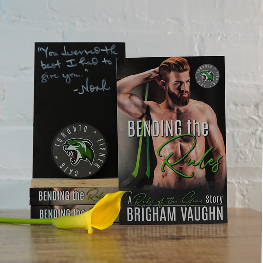 Signed paperback book titled 'Bending the Rules' by Brigham Vaughn with a yellow flower on a wooden surface.