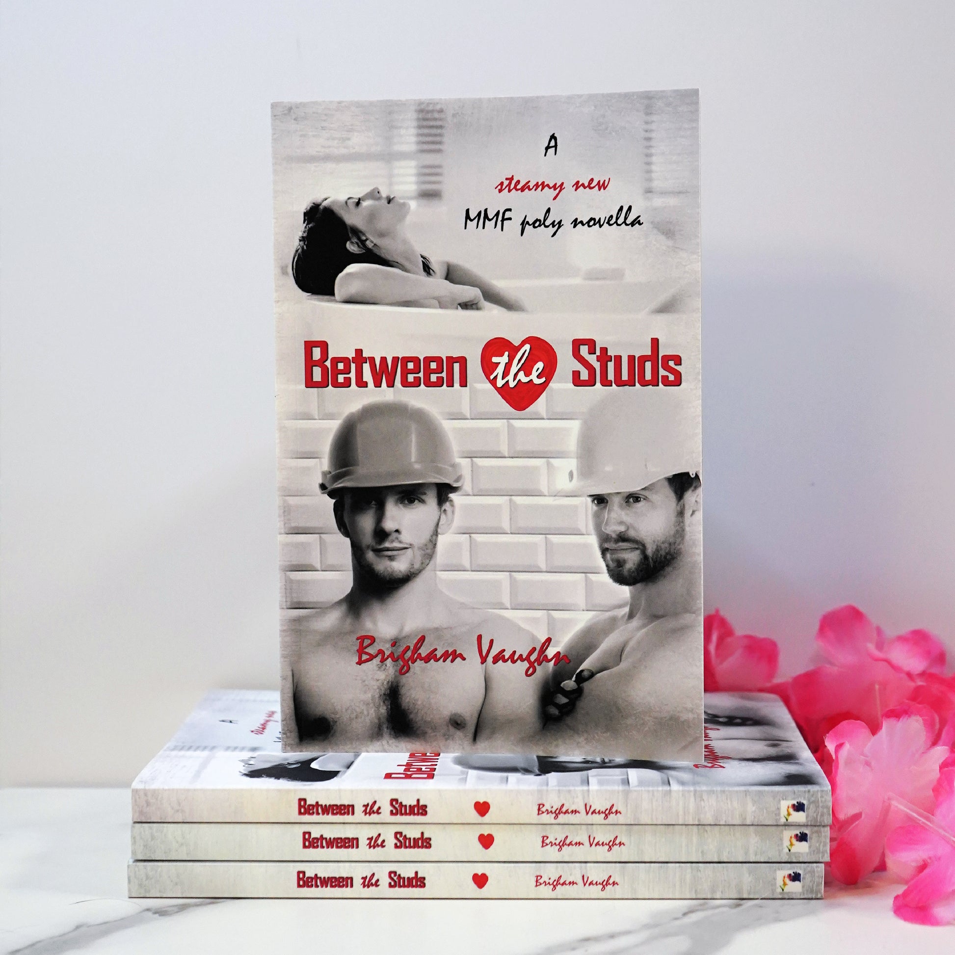 Signed paperback book titled 'Between the Studs' by Brigham Vaughan with a pink flower against a white wall. 