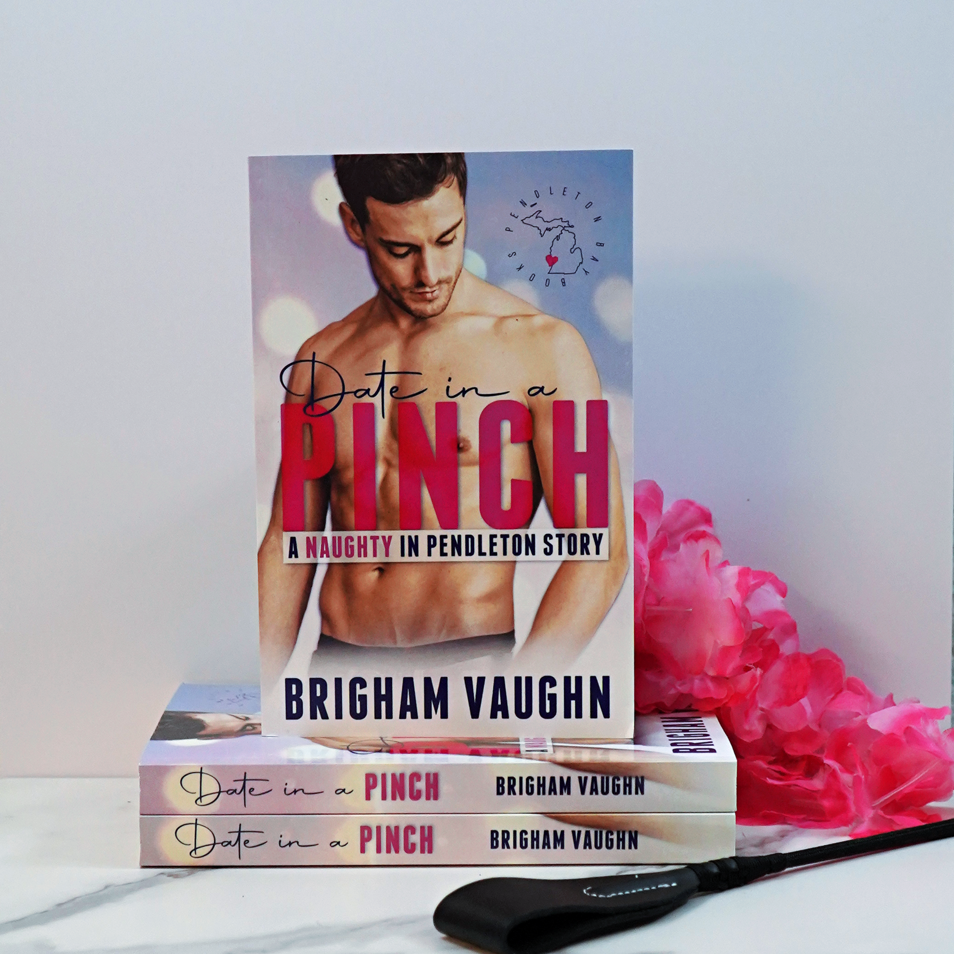 Stack of paperback books titled 'Date in a Pinch' by Brigham Vaughn with a pink flower on a white surface.