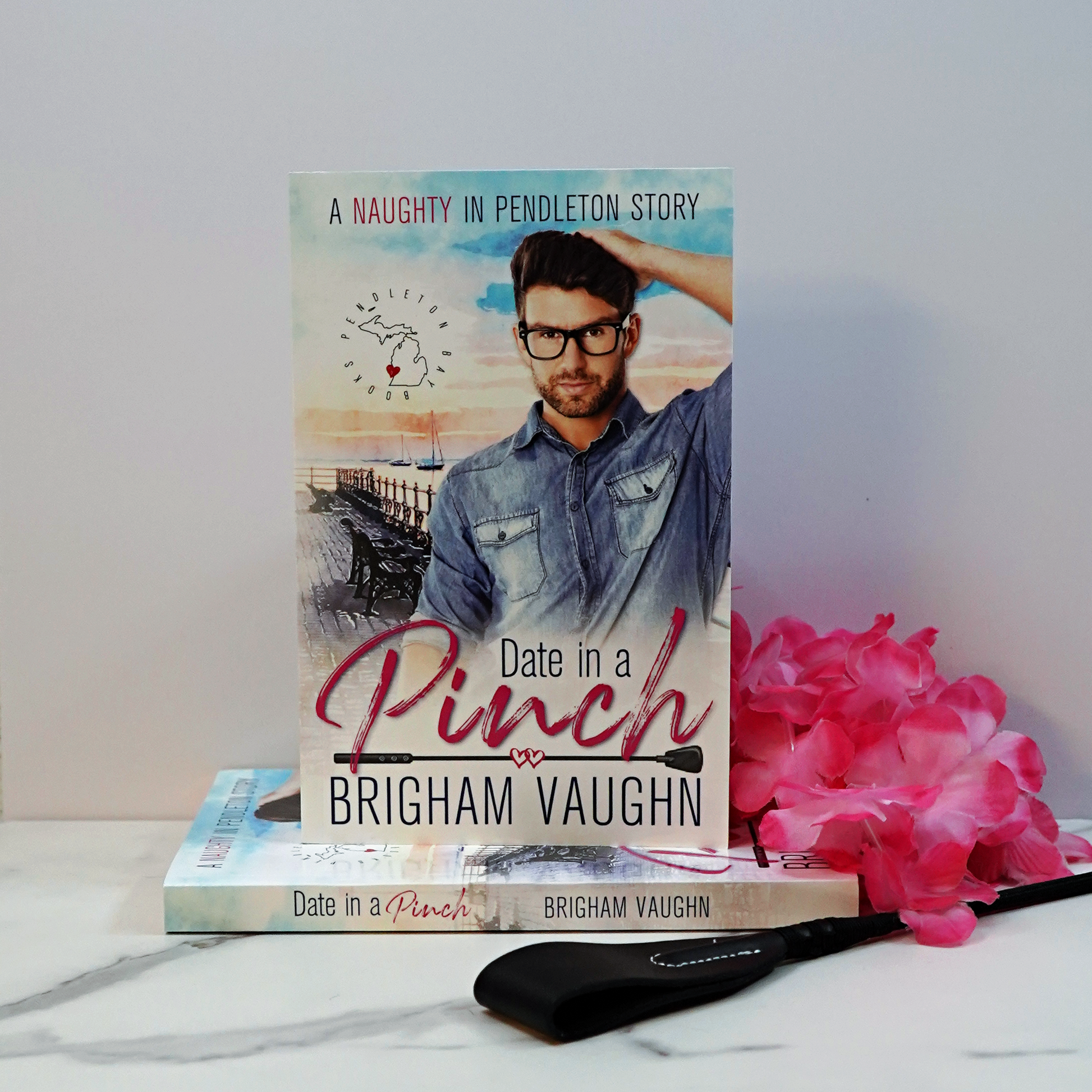 Stack of paperback books titled 'Date in a Pinch' by Brigham Vaughn with a pink flower and a riding crop on a white surface.