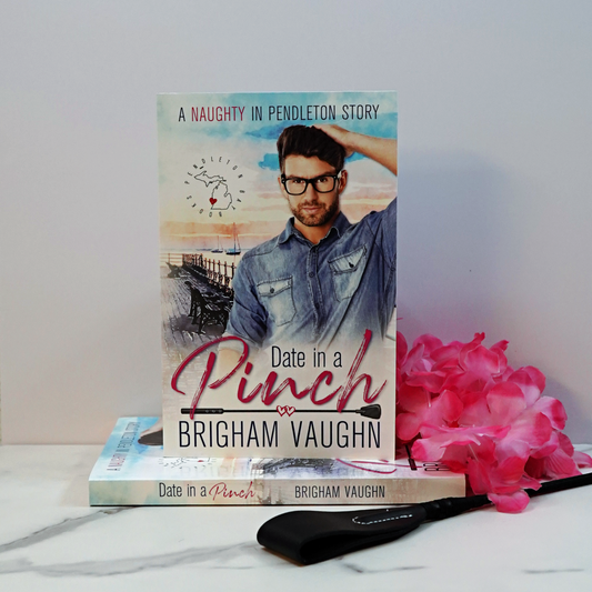 Stack of paperback books titled 'Date in a Pinch' by Brigham Vaughn with a pink flower and a riding crop on a white surface.