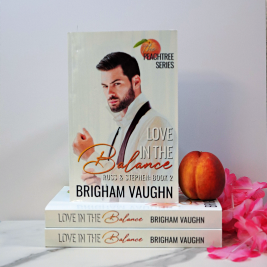 Stack of signed paperback books titled 'Love in the Balance' by Brigham Vaughn with a peach and pink flower on a white surface.