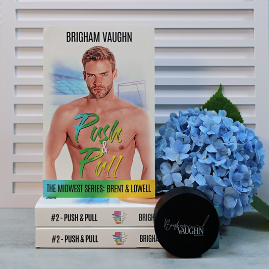 Signed paperback books titled 'Push & Pull' by Brigham Vaughnr, surrounded by blue flowers and a hockey puck.
