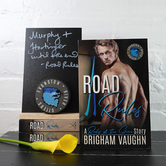 Signed paperback book titled 'Road Rules' by Brigham Vaughn with a yellow flower on a white brick wall background