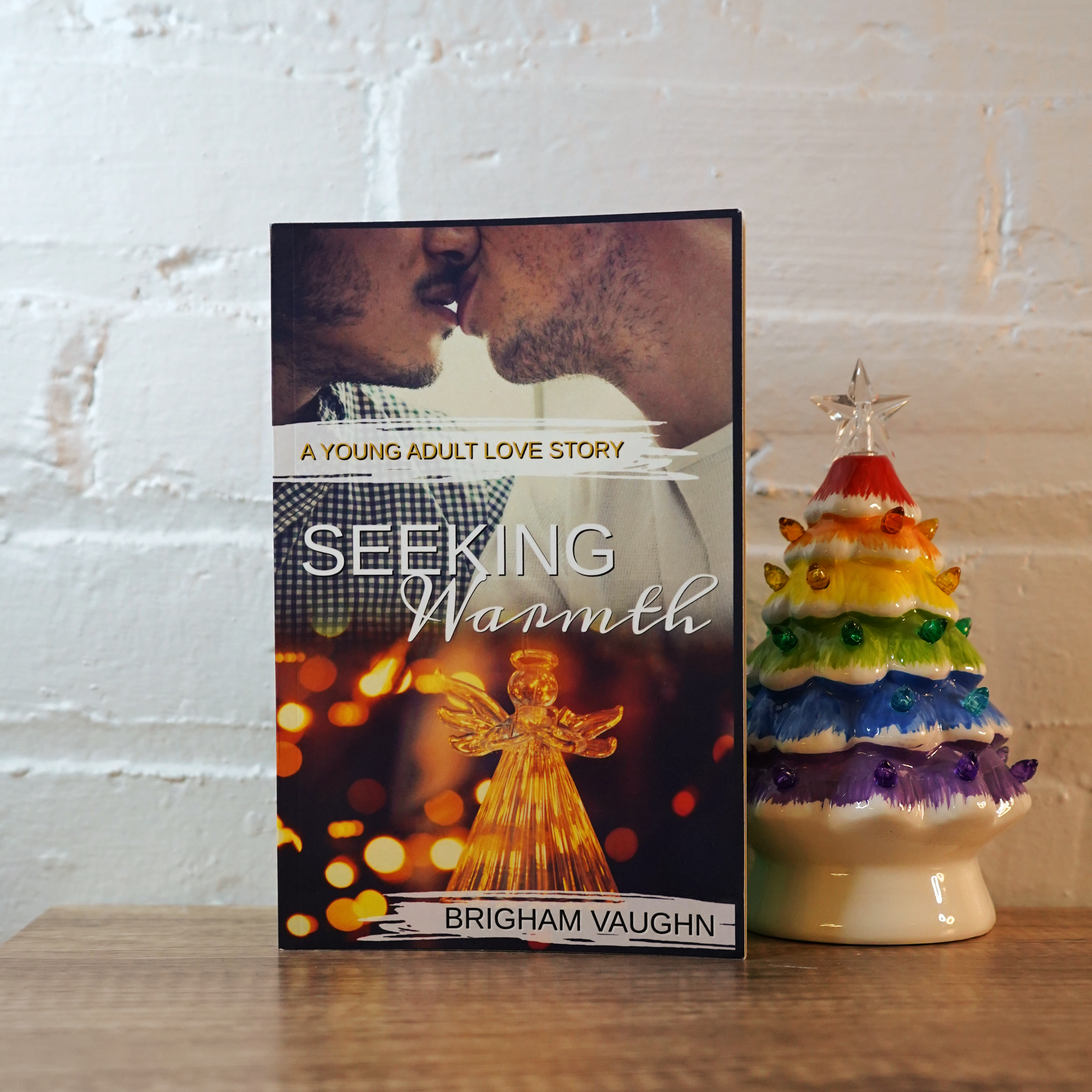 Signed paperberback book titled 'Seeking Warmth' by Brigham Vaughn next to a colorful ceramic tree on a wooden surface.