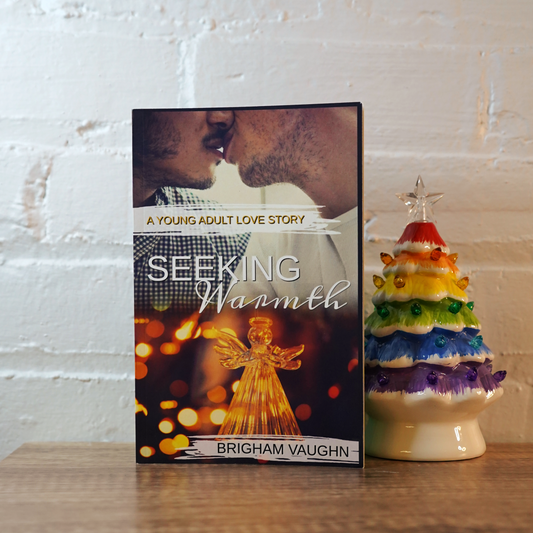 Signed paperberback book titled 'Seeking Warmth' by Brigham Vaughn next to a colorful ceramic tree on a wooden surface.