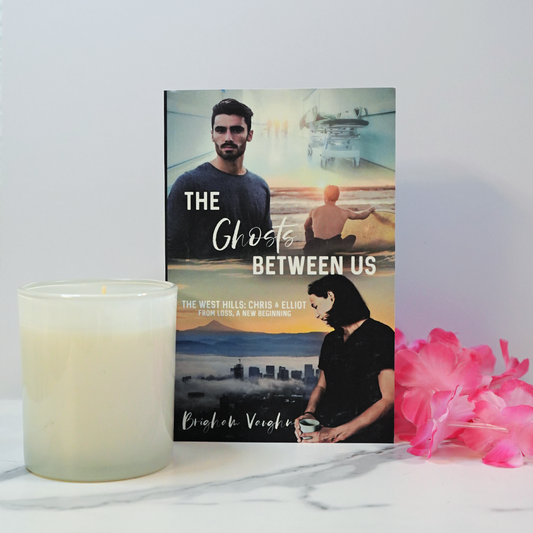 Signed paperback book titled 'The Ghosts Between Us' with a candle and pink flowers on a white surface.