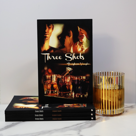 Signed paperback books titled 'Three Shots' by Brigham Vaughan with a glass of whiskey on a marble surface.
