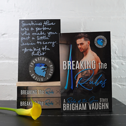 Signed paperback book titled 'Breaking the Rules' by Brigham Vaughn with a quote card and yellow flower against a white brick wall background.