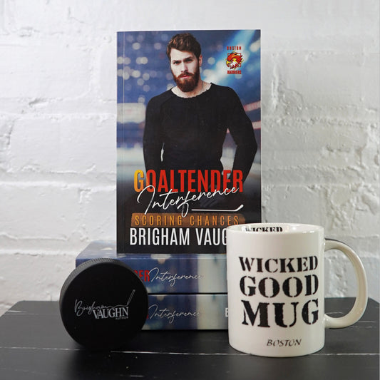 Signed paperback book titled 'Goaltender Interference' by Brigham Vaughn with a mug and hockey puck on a white brick wall background.