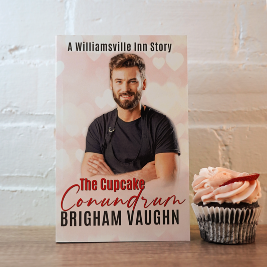 Signed paperback book titled 'The Cupcake Conundrum' by Brigham Vaughn with a cupcake in front of a white brick wall. 